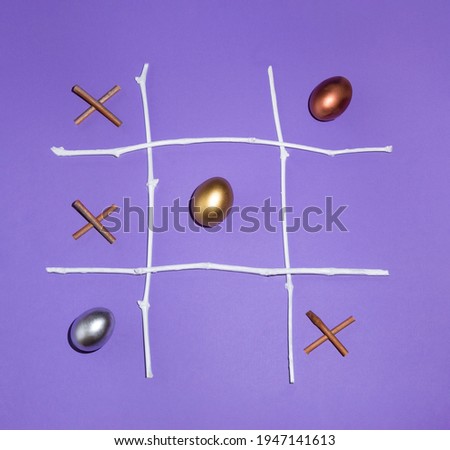 2021 Easter eggs are a winning combination. X O game made of golden, silver and bronze eggs and natural twigs on purple background. Creative tic tac toe game idea. 