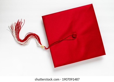 2021 - Flat lay of a red graduation cap with a white and red tassel and gold bobble, isolated on white, Toronto, Ontario, Canada.