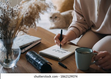 2021 Goals, New Year Resolution, Planning. Woman Writing In Notebook With Text 2021 Loading On The Table In Apartments With Cat. Selective Focus