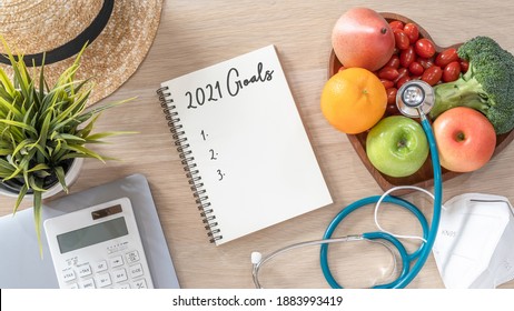 2021 Goals On Note Book For New Year List Reminder In Notebook Of Yearly Planner And Health Plan For Work-life Balance On Desk Background Of Computer, Healthy Food, Face Mask For Covid-19 Protection 