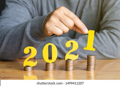 2021 New Year Saving Money And Financial Planning Concept. Female Hands Putting Gold Wooden Number 2021 On Stack Of Coins. Tax Payment, Investment And Banking.