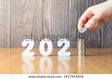 2021 New year saving money and financial planning concept. Hand putting coins on stack with 2021 number on wooden table. Creative idea for business growth, tax payment, investment and banking.