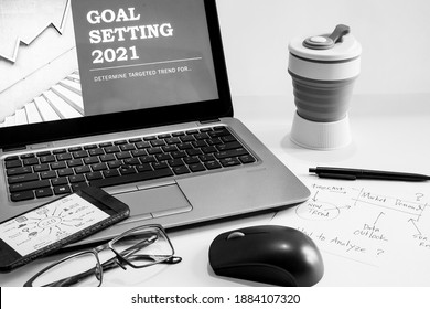 2021 Office desk and presentation devices with notebook, mouse computer, paper note for Goal Setting, eye glasses and tumblr. Concept for business plan on Black and white photo