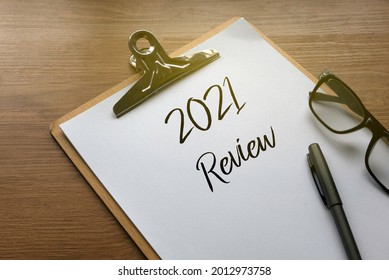 2021 review with clipboard,pen, glasses and paper on wooden background.