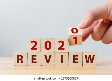 2021 review concept. Hand flip wood cube change year 2020 to 2021 and the word REVIEW on wooden block on wood table
