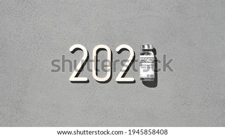 The 2021 - year of mass vaccination against COVID-19 of world population, the concept of victory over coronavirus. Overhead view of 2021 date and vial with vaccine on gray background