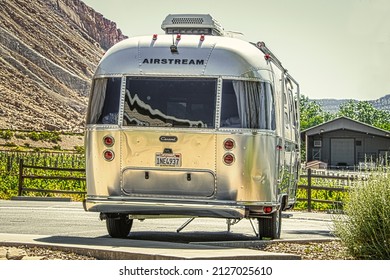 2021_06_04 Grand Junction Colorado USA - Airstream camper trailer parked on concrete with grape vineyards and mesa and barn behind it.