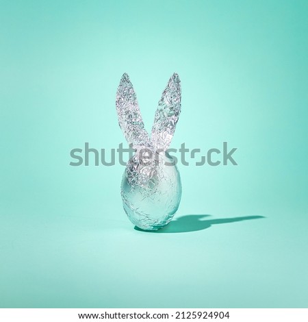 2022 Easter minimal concept. Egg in aluminium foil with rabbit ears and shadow on blue green background. Unique spring holiday idea. 