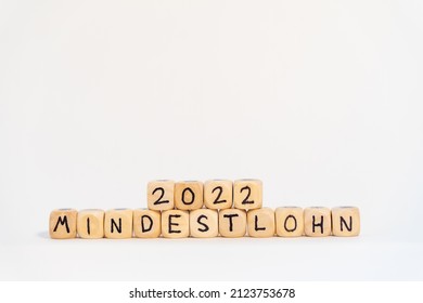 2022 German Word For Minimum Wage, MINDESTLOHN, Spelled With Wooden Letters Wooden Cube On A Plain White Background , Concept Image 