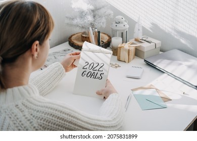 2022 goals, New year resolution. Woman in white sweater writing Text 2022 goals in open notepad on the table. Start new year, planning and setting goals for the next year
