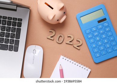 2022 and laptop, Piggy bank, calculator on brown background. Economy, new year composition. Budget, plan of the year