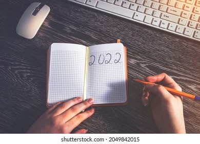 2022 plans for the new year, in the hands of the girl's diary in a cage and a pen. Keyboard and mouse in the background