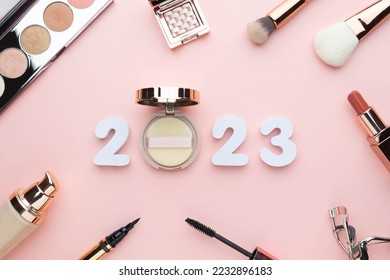 2023 Beauty cosmetic makeup products trends concept. Top view of 2023 white number with powder, lipstick, foundation, eyeshadow, brush, eyeliner and mascara on pink background. - Shutterstock ID 2232896183