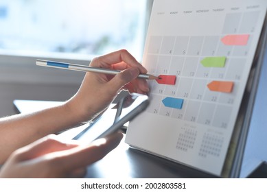 2023 Event planner timetable agenda plan on schedule event. Business woman checking planner on mobile phone, taking note on calendar desk on office table. Calendar event plan, work planning