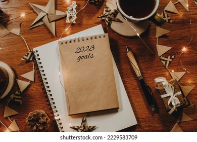 2023 goals written in notebook on wooden table with Christmas decorations, pen and cup of tea. New Year's resolutions, setting goals for next year. Planning concept with copy space. Creative flat lay