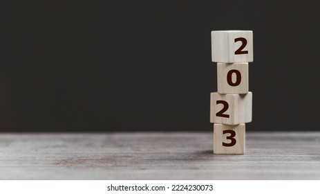 2023 Happy New year background banner. Two thousand Twenty-Three year numbers on wooden cube blocks stack on dark  background with copy space. Welcome, Merry Christmas, and Happy New Year in 2023.