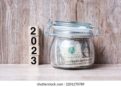2023 Happy New Year with US dollar money glass American on wood table background. business, investment, retirement planning, finance, Saving and New Year Resolution concepts