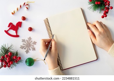 2023 New Year's resolutions with Christmas decorations. Woman's hand writing in empty notebook. Top view, flat lay, copy space. Christmas, New Year.