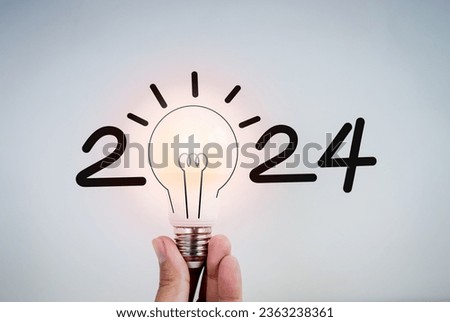 2024 calendar year numbers, handwritten decorated with creative trend fun style on glowing lightbulb holding by hand on white background. Happy 2024 New Year, cool greeting card with light bulb.