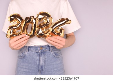 2024 - New Year concept. Female hands hold a gold colored inflatable foil balloons in front of blue background. 