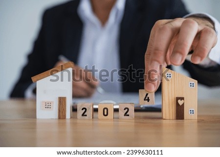 2024 new year target home loan trends. Businessman hold model house and wood blocks word LOAN. plan finances investments and savings to buy house real estate. Home accounting and tax and insurance.