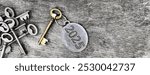 2025 engraved on a ring of an old golden  key next to a group fo silver old keys on wooden background 