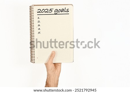 2025 goals written on a notebook held by a man. Isolated on white background.