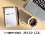 A 2025 goal-setting setup with a notebook, black coffee cup, and pen arranged on a wooden table, top view with copy space.