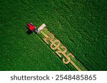 2025 Happy Ney Year text on the ground and tractor mowing green field aerial view