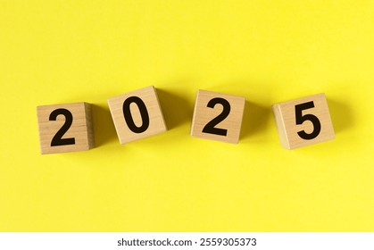 2025 new year, text numbers on wood cube blocks on yellow background.