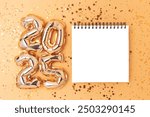 2025 New Year wish list concept. Empty notepad mockup, shiny stars confetti and golden numbers foil balloons.