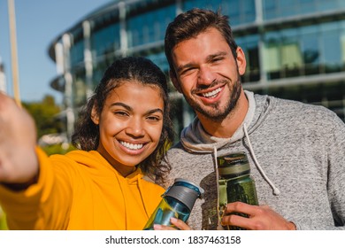 20s Mixed Race Happy Couple Taking Selfie After Jogging Holding Bottles Of Water In Urban Area