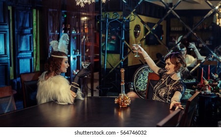 20s style concept. Two pretty ladies in vintage dresses dancing and drinking in old-fashioned interior. Having fun 