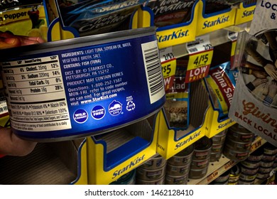 O’fallon, IL—July 21, 2019; Illustrative Editorial Of Canned Tuna With Dolphin Safe Certification Logo On The Side Of The Can In Hand With Shelf Full Of Other Consumer Packaged Goods In Background.