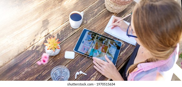 21 April, 2021. Cyprus, Kyrenia, Sinir Sokak Street. .Woman Searching Inspiration In Pinterest On A Digital Tablet And Writing Notes,drinking Coffee At The Home Garden Office.