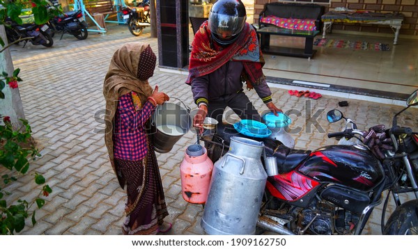 21 January 2021- Badhal, Jaipur, India. An Indian\
woman pouring out milk to milkman. Milk man measuring the milk with\
Liter cane.