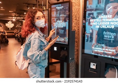 21 July 2022, Dusseldorf, Germany: Woman Customer Wearing Face Mask Uses A Terminal Or Self-service Kiosk To Order At A Fast Food Restaurant.