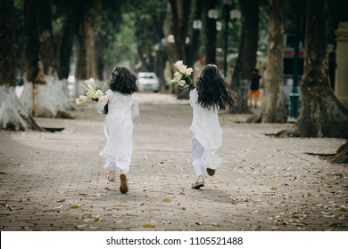 211/5000
Two little girls dressed in traditional Vietnamese costume on the road with beautiful trees at sunset in Hanoi, Vietnam.