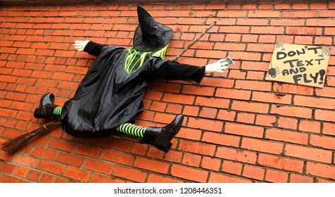 21st October 2018, Dublin, Ireland.  Halloween witch with a broom on a wall holding a mobile phone with a sign next to her saying Don't text and fly. 