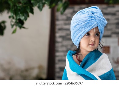 22 Months Old Cute  Indian Baby Girl Wearing Blue Hair Towel Wrap Turban And Body Wrapped With Blue And White Towel, Sandalwood Anoint On Her Forehead Sitting And Looking Side Wise.