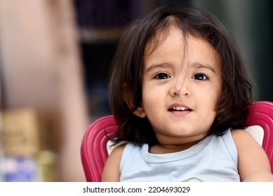 22 Months Old Cute  Indian Baby Girl Wearing Aqua Color T-shirt Sitting On A Baby Pink Color Chair And Giving Cute Expressions