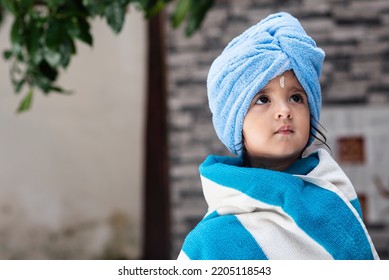 22 Months Old Cute  Indian Baby Girl Wearing Blue Hair Towel Wrap Turban And Body Wrapped With Blue And White Towel, Sandalwood Anoint On Her Forehead Sitting And Looking Up