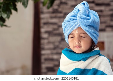 22 Months Old Cute  Indian Baby Girl Wearing Blue Hair Towel Wrap Turban And Body Wrapped With Blue And White Towel, Sandalwood Anoint On Her Forehead Sitting With Eyes Closed Smiling Expressions.