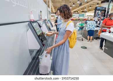 23 February 2021, Dubai, UAE: woman wearing face mask scans her supermarket purchases at a self-service checkout to make it safer to avoid contact with sellers and cash during coronavirus pandemic