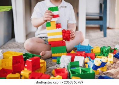 A 2-3 year old boy plays with colored plastic construction blocks sitting on the floor in a room against a white wall. child development and creativity. unrecognizable without face close-up
