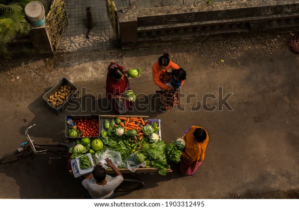 23rd January 2021 Kolkata, west\
Bengal, India: A vegetable seller selling vegetables door to door\
on his cycle van and three house wives buying from\
him.