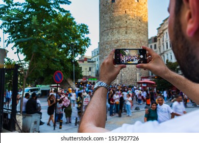 24 August 2019; Galata Tower, Istanbul, Turkey; A Young Bearded Man Taking Picture Of A Crowd Of People At Famous Turkish Landmark On His Iphone X On A Sunny Day