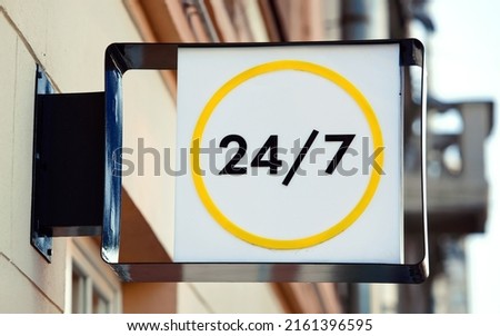 24 hours open sign or working around the clock sign hanging on wall. Working 24 hours, sign on facade of building.