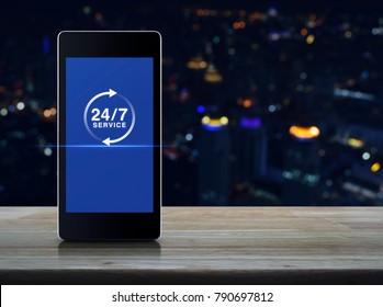 24 Hours Service Icon On Modern Smart Phone Screen On Wooden Table Over Blur Colorful Night Light City Tower, Full Time Service Concept