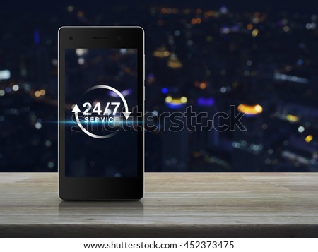 24 hours service icon on modern smart phone screen on wooden table over blur light city tower background, Full time service concept